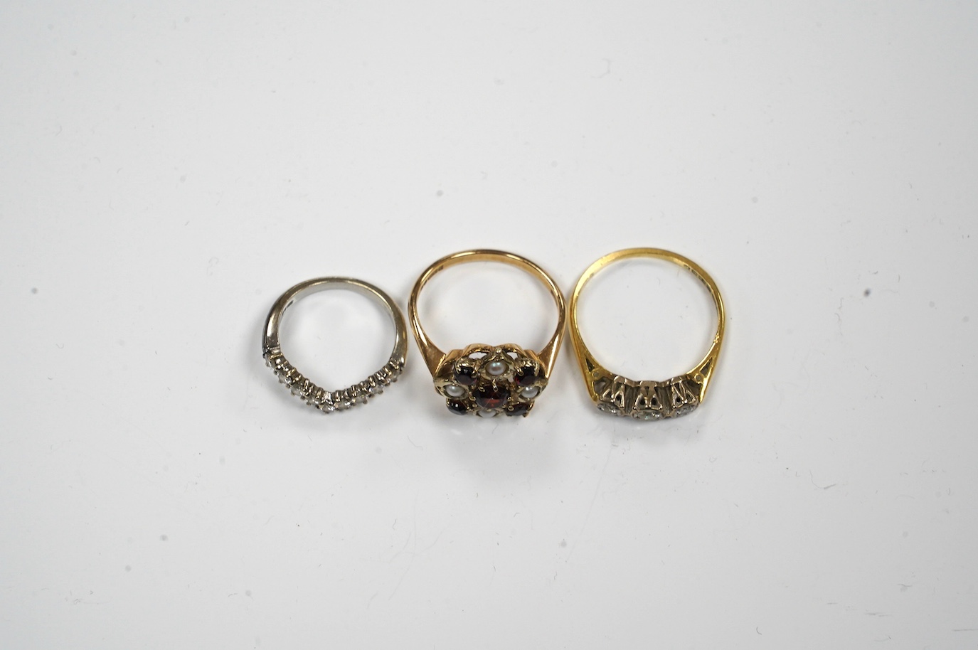 Two 18ct gold and diamond set rings including chevron shape and a 9ct gold, garnet and seed pearl set ring. Condition - fair